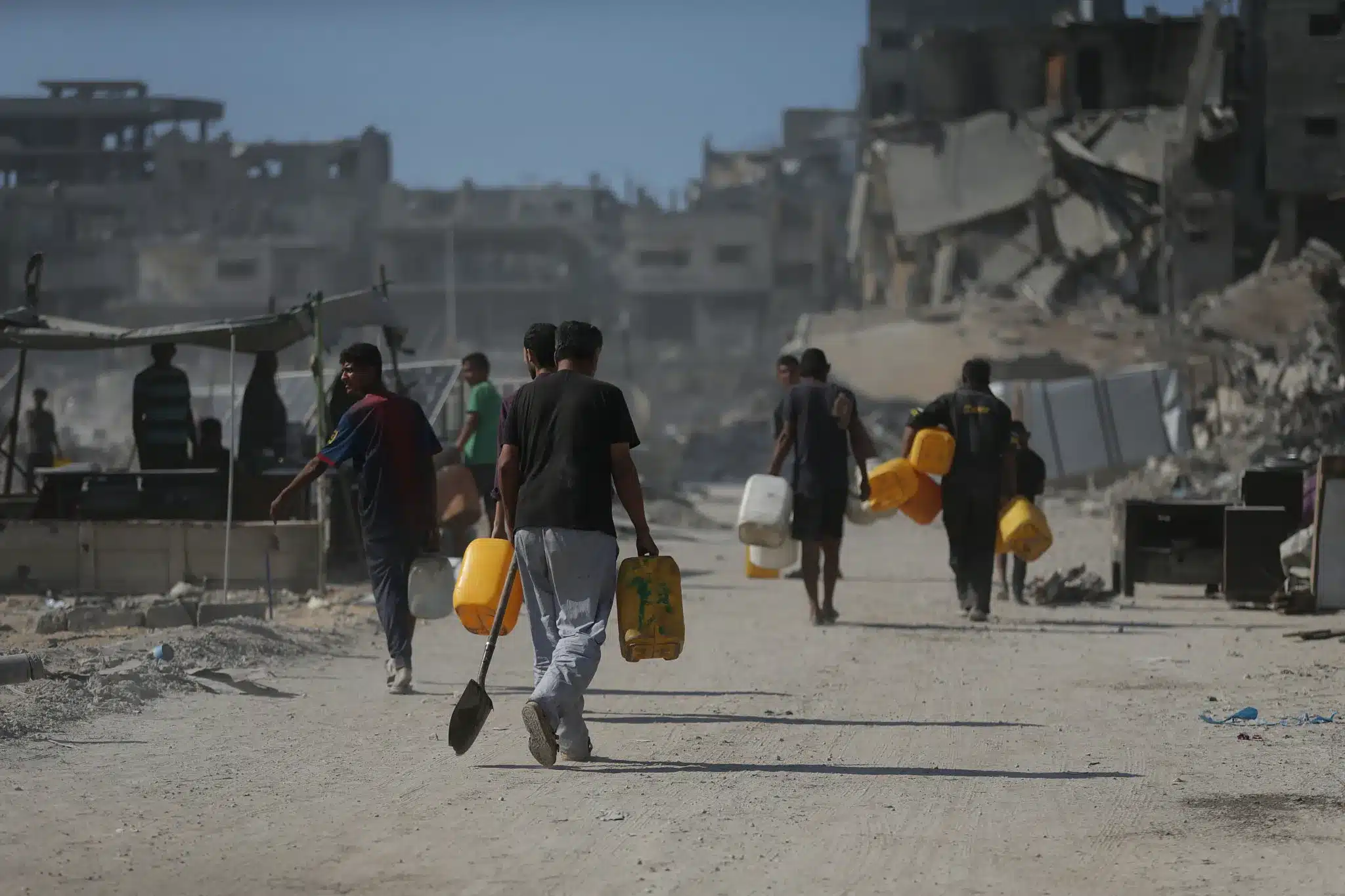 Palestinos cargan cántaros en busca de agua entre los escombros de Jabalia, norte de Gaza, 16 de octubre de 2025. (Yousef Zaanoun)