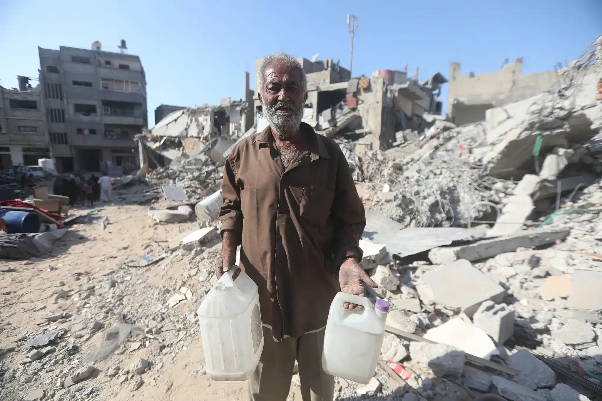 Jamal Atta Abu Tabeikh se encuentra entre las ruinas de su barrio destruido de Sheikh Radwan en la ciudad de Gaza, cargando recipientes de agua vacíos. (Yousef Zaanoun)