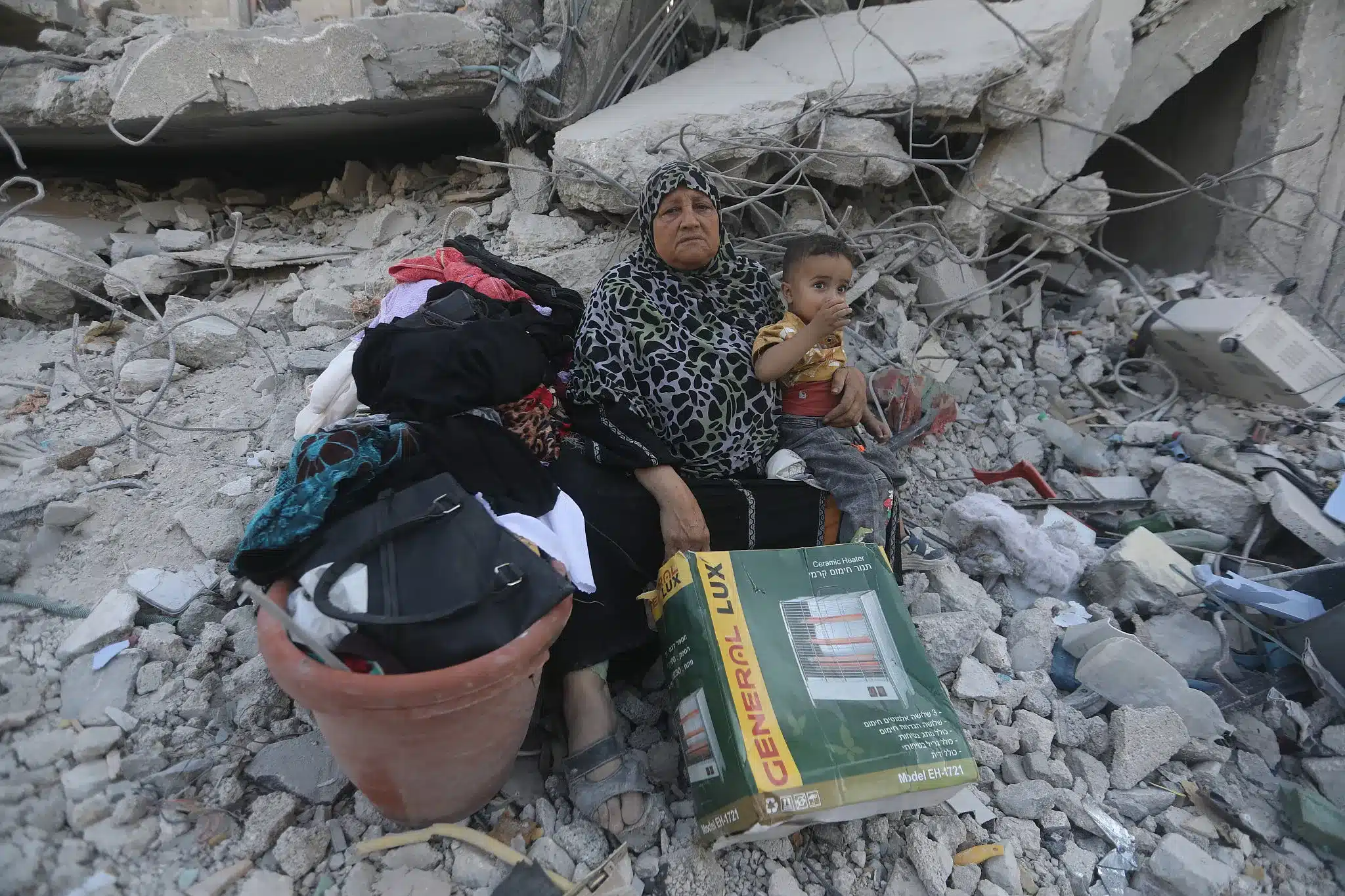 Umm Saeed Abu Warda se sienta entre los escombros de su casa destruida en Jabalia, sosteniendo a su nieto pequeño. (Yousef Zaanoun)